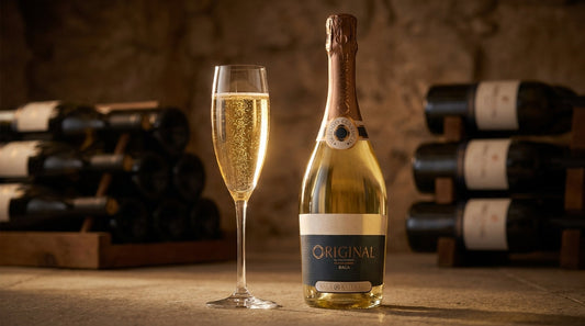 Glas Bairrada-Schaumwein mit feiner Perlage neben der Flasche Original Espumante Baga im Kalksteinkeller