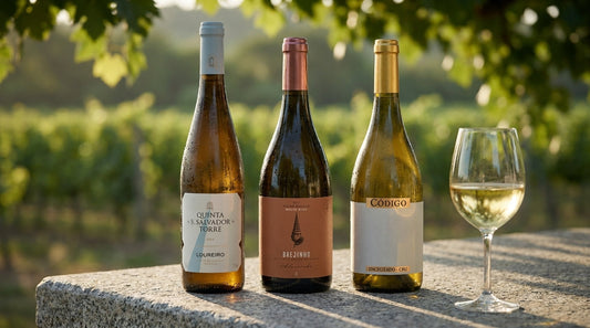 Drei portugiesische Weissweine mit Loureiro, Alvarinho und Encruzado auf einem Granittisch vor Rebzeilen