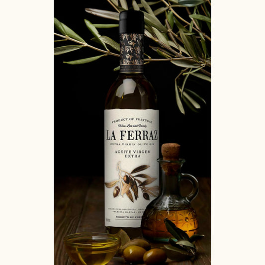 LA Ferraz Olivenöl Flasche mit Oliven und offenem Olivenöl im Vordergrund und Olivenbaumzeigen im Hintergrund